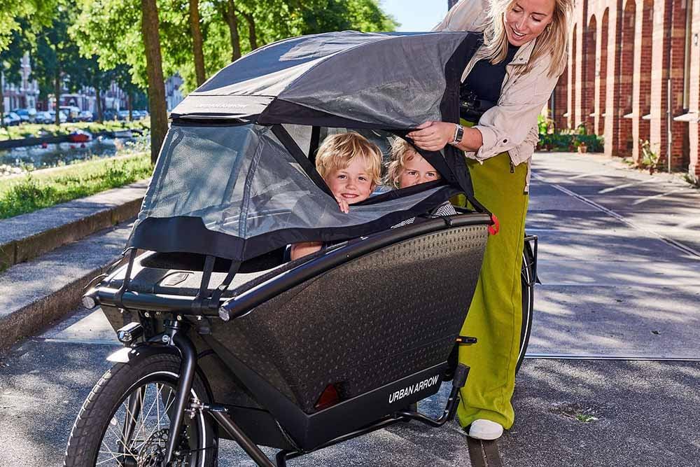 Frau mit zwei Kindern in einem Urban Arrow Lastenrad auf einer sonnigen Straße
