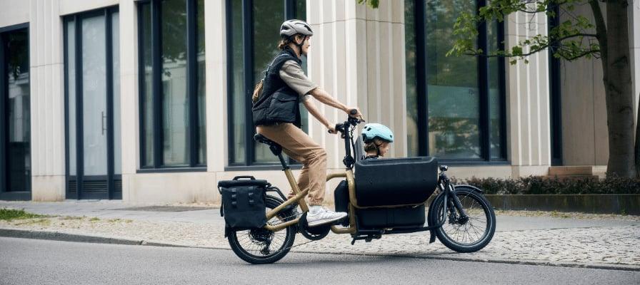 Mann fährt Riese & Müller Lastenrad mit Kindersitz auf Stadtstraße