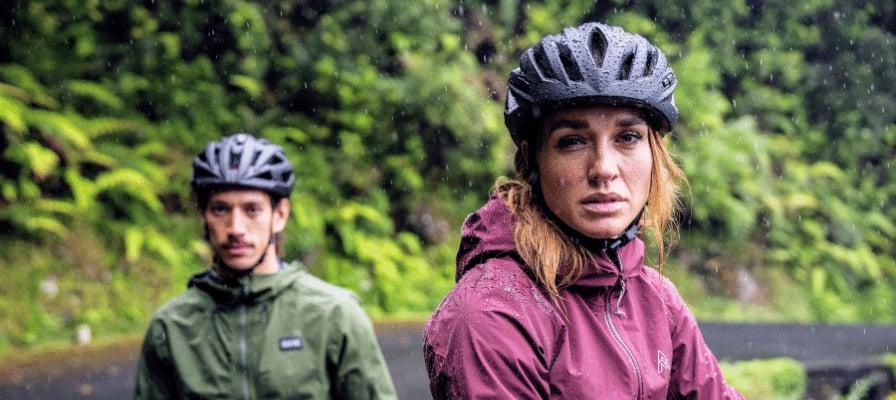 Zwei Personen mit Fahrradhelmen im Regen vor grüner Waldkulisse
