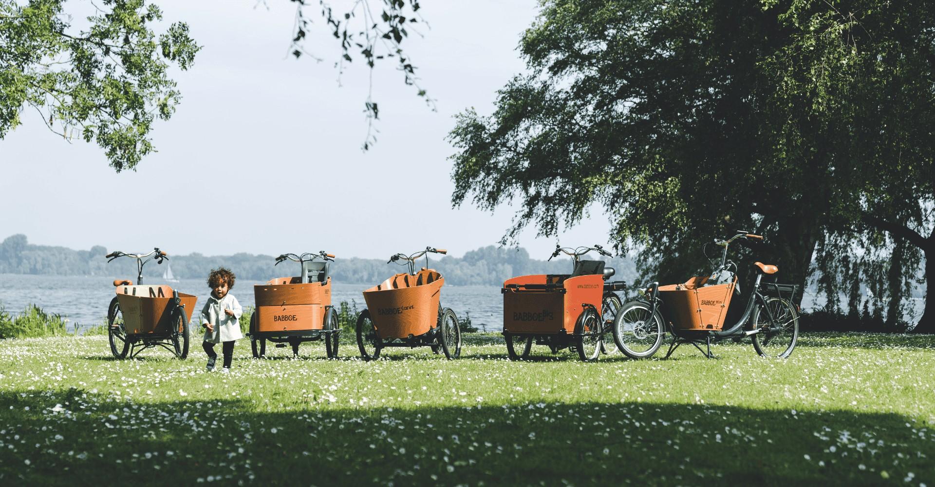 Ein Kind steht neben verschiedenen Babboe Lastenfahrrad-Modellen