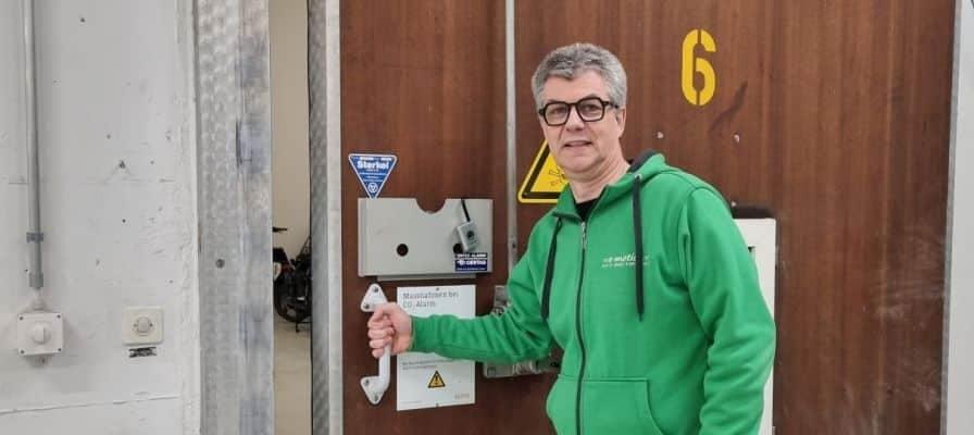 Mann in grüner Jacke öffnet große Holztür mit Schild