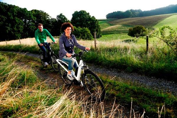 Zwei Personen fahren E-Bikes auf einem ländlichen Weg durch grüne Landschaft