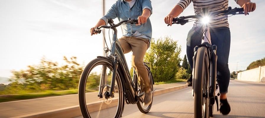 Zwei Personen fahren auf modernen E-Bikes auf einer Straße bei Sonnenuntergang