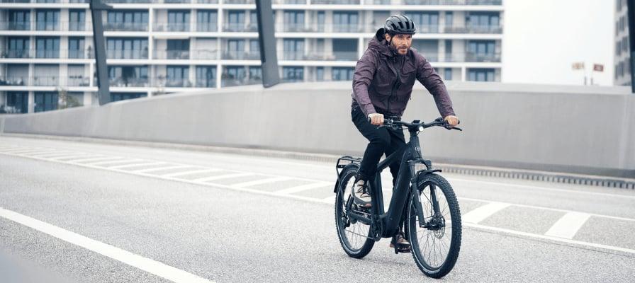Mann auf E-Bike fährt über moderne Brücke in urbaner Umgebung