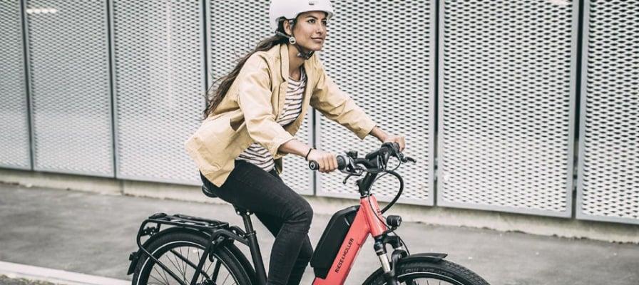 Frau auf E-Bike mit rotem Rahmen fährt vor Metallzaun