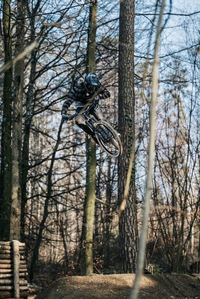 Mountainbiker springt im Wald über Erdhügel