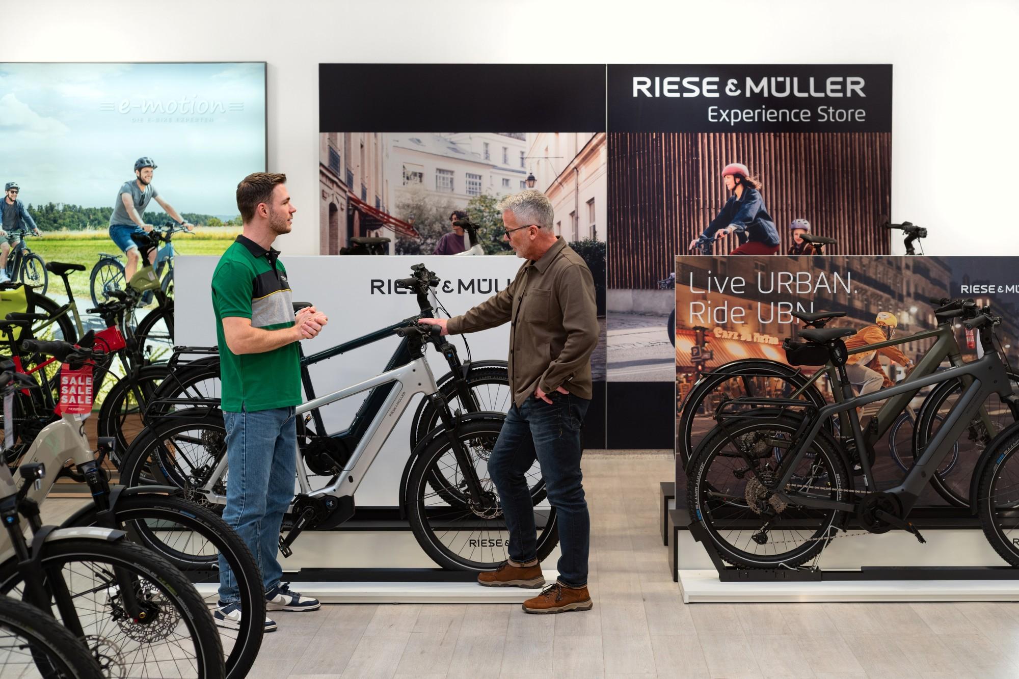 Das Bild zeigt eine Beratungssituation im Riese & Müller Experience Store, wo ein Verkäufer einem Kunden Informatio