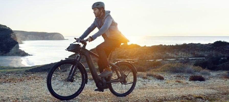 Mann fährt Riese & Müller Charger3 E-Bike am Strand bei Sonnenuntergang