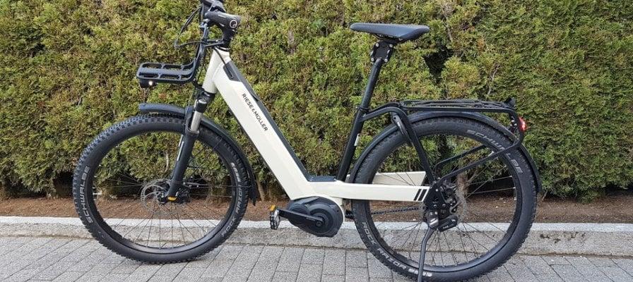 Weißes E-Bike von Riese & Müller vor grüner Hecke