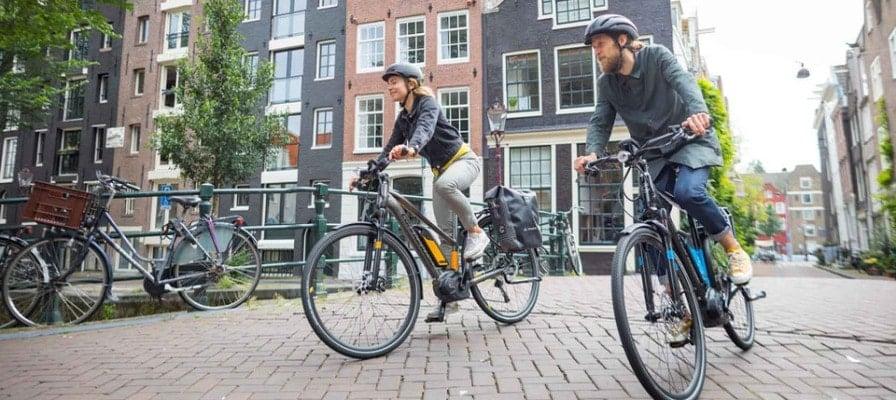 Zwei Personen fahren auf E-Bikes durch eine Stadtstraße