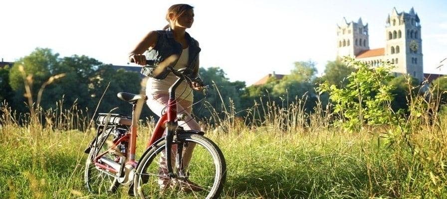 Frau mit E-Bike in sonniger Landschaft vor historischer Kulisse