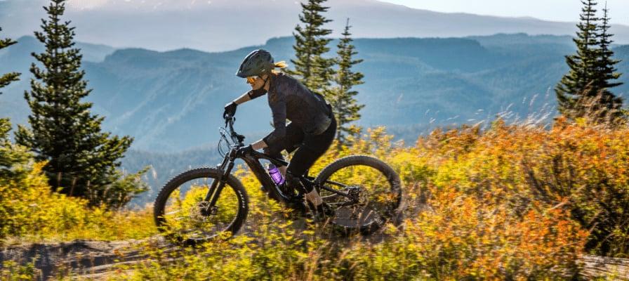 Mountainbikerin fährt auf Waldweg in bergiger Landschaft