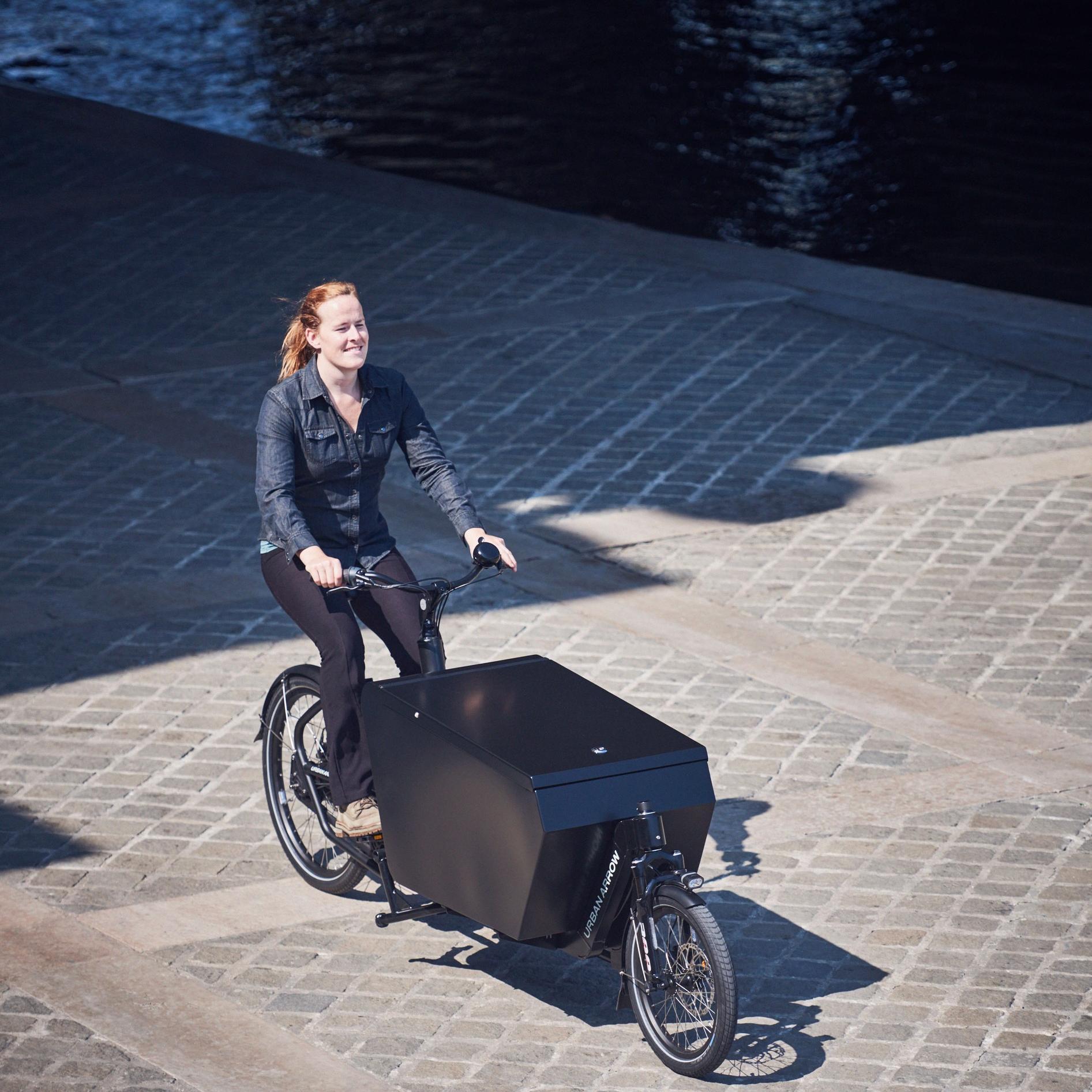 Eine Frau bringt gerade auf einem Urban Arrow Lastenrad Waren zu einem Geschäft in Köln.
