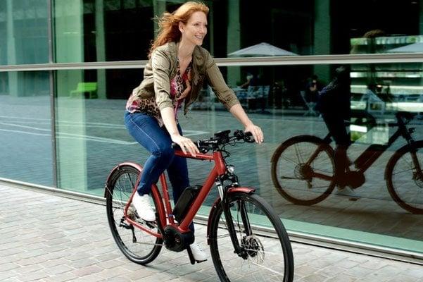 Frau fährt rotes E-Bike vor spiegelnder Glasfassade