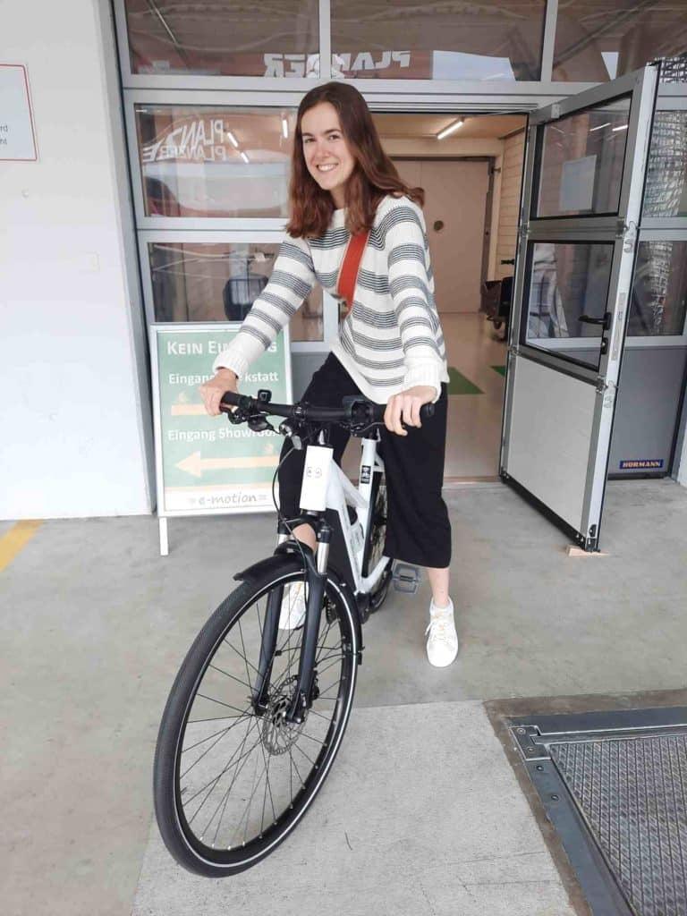 Frau auf E-Bike verlässt Geschäft durch geöffnete Tür