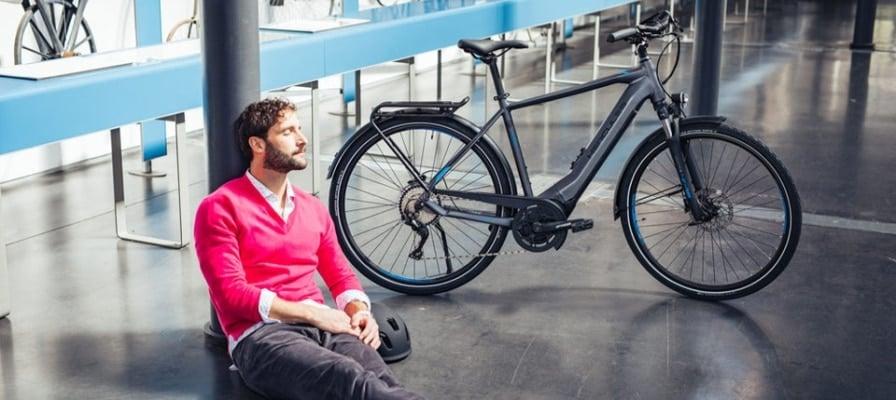 Mann entspannt sich neben E-Bike in modernem Innenraum