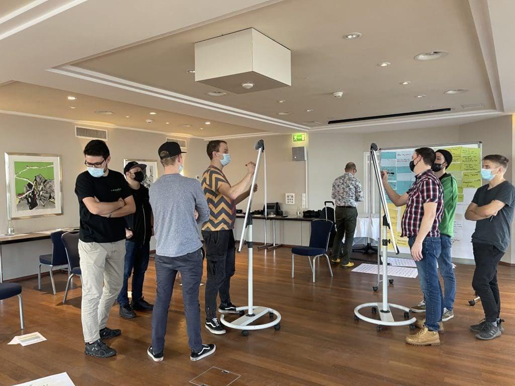 Menschen in einem Meetingraum mit Flipcharts und Masken