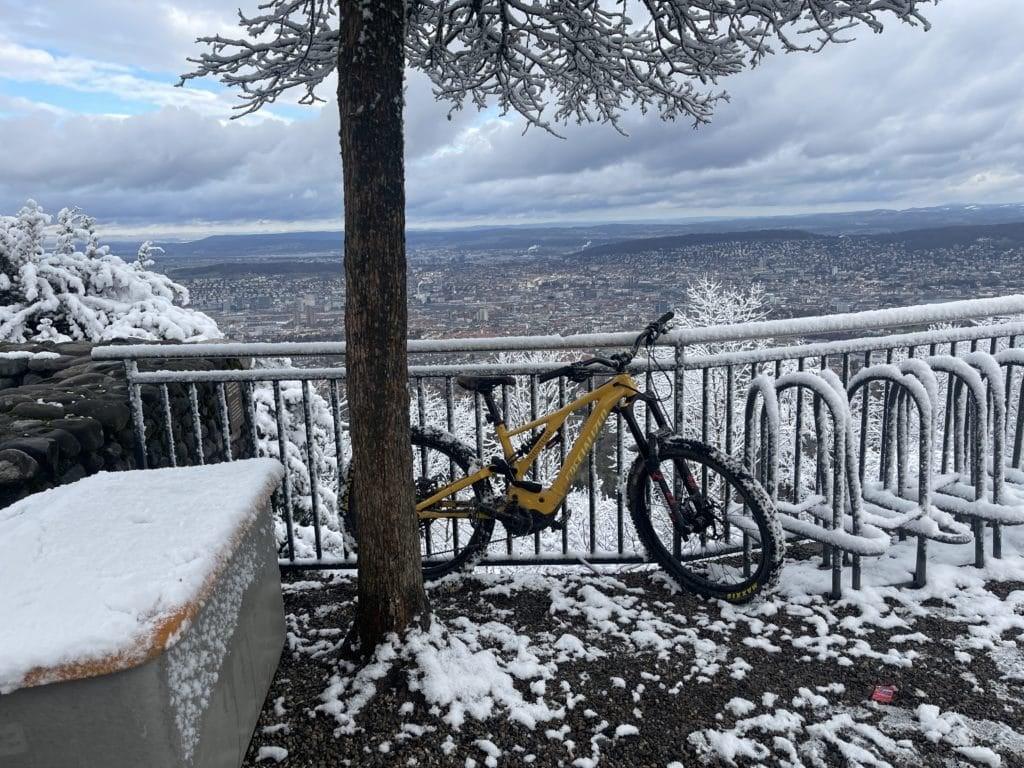 Gelbes Fahrrad an verschneitem Aussichtspunkt mit Stadtblick