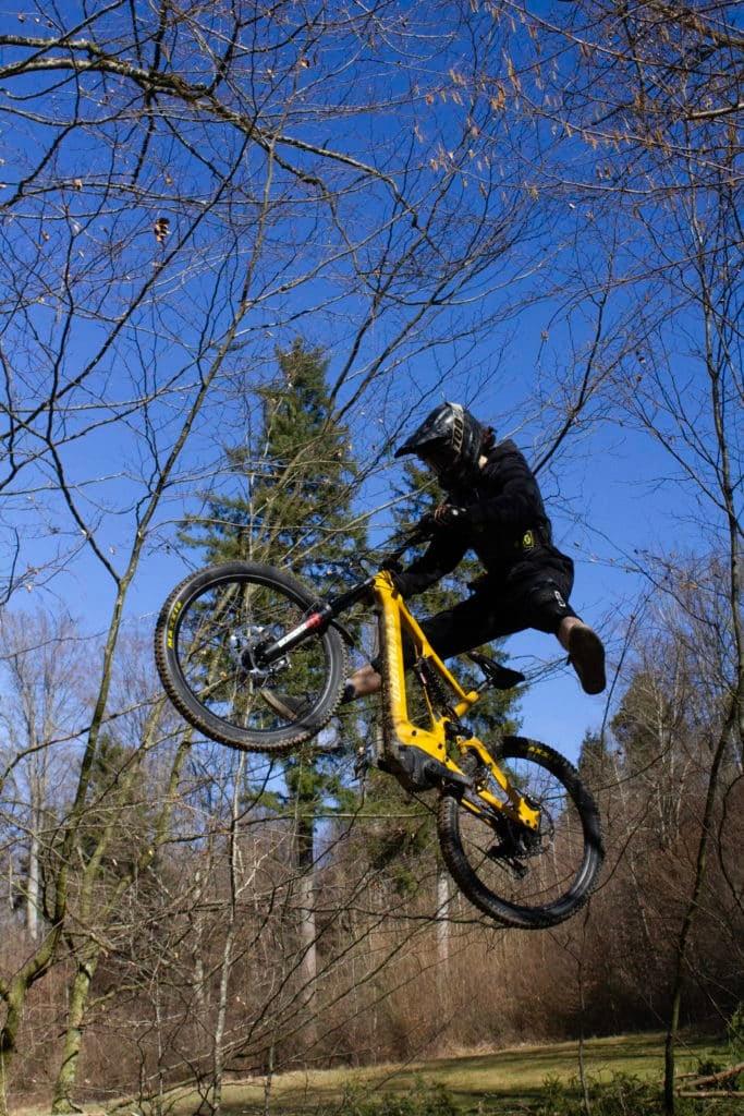 Mountainbiker springt mit gelbem E-Bike durch Waldlandschaft