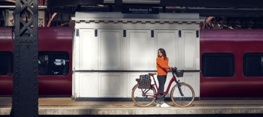 Frau mit E-Bike auf Bahnsteig vor rotem Zug