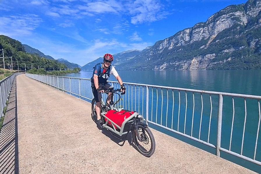 Mann auf E-Bike mit Anhänger fährt entlang eines Sees