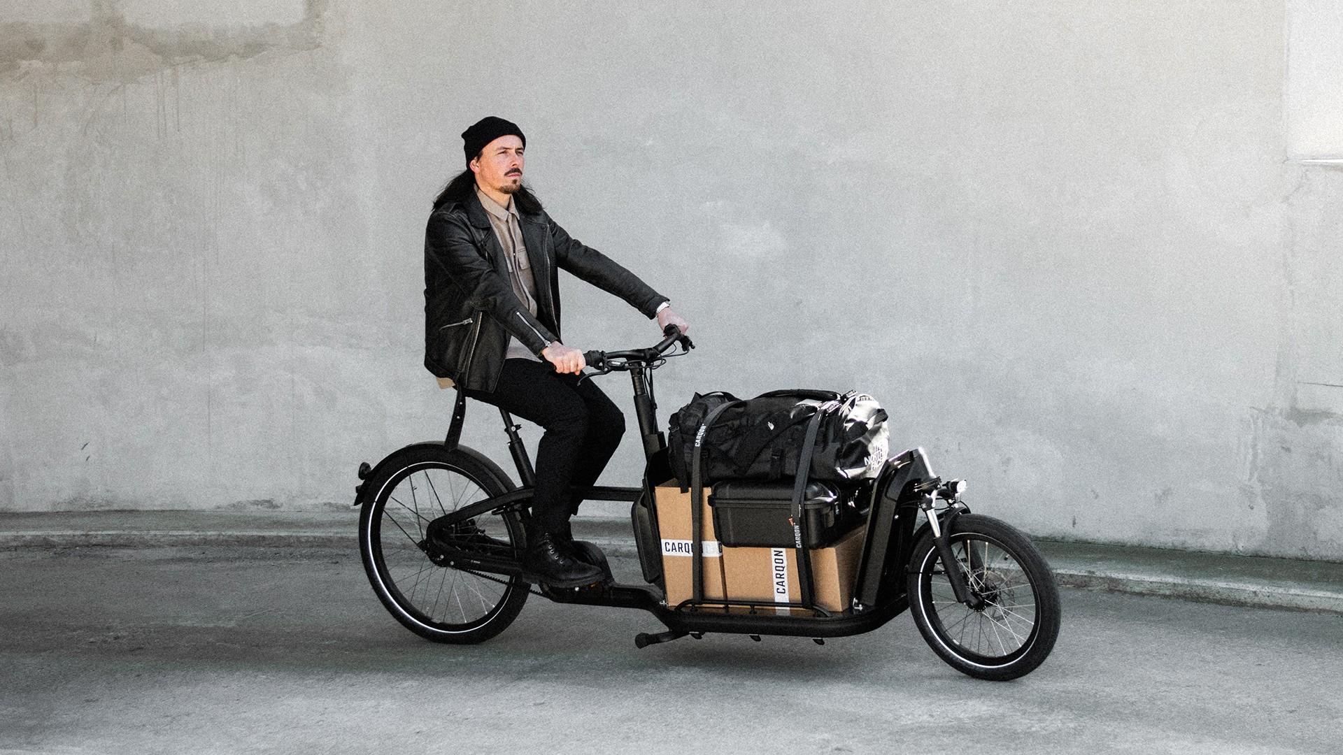 Ein Mann fährt mit einem vollgepackten Lastenrad, dem Carqon Flatbed, durch die Straßen