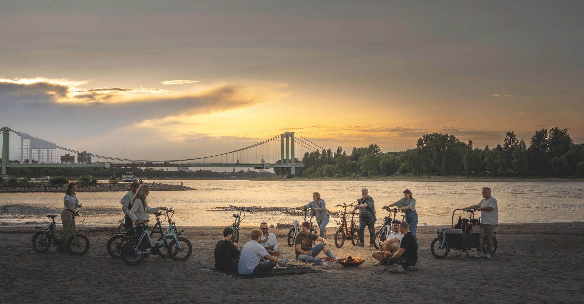 Eine Gruppe steht und sitzt zusammen am Rhein mit verschiedenen i:SY e-Bike Modellen