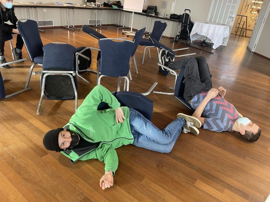 Zwei Personen liegen auf umgekippten Stühlen in einem Raum