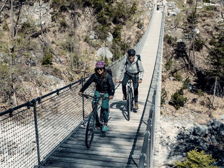 Zwei Personen fahren mit e-Bikes über eine Hängebrücke