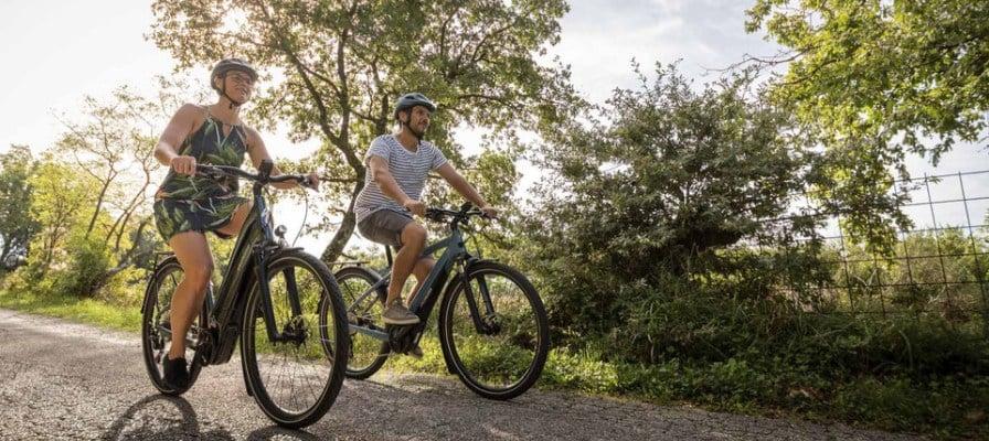Zwei Personen fahren E-Bikes auf einem ländlichen Weg bei sonnigem Wetter