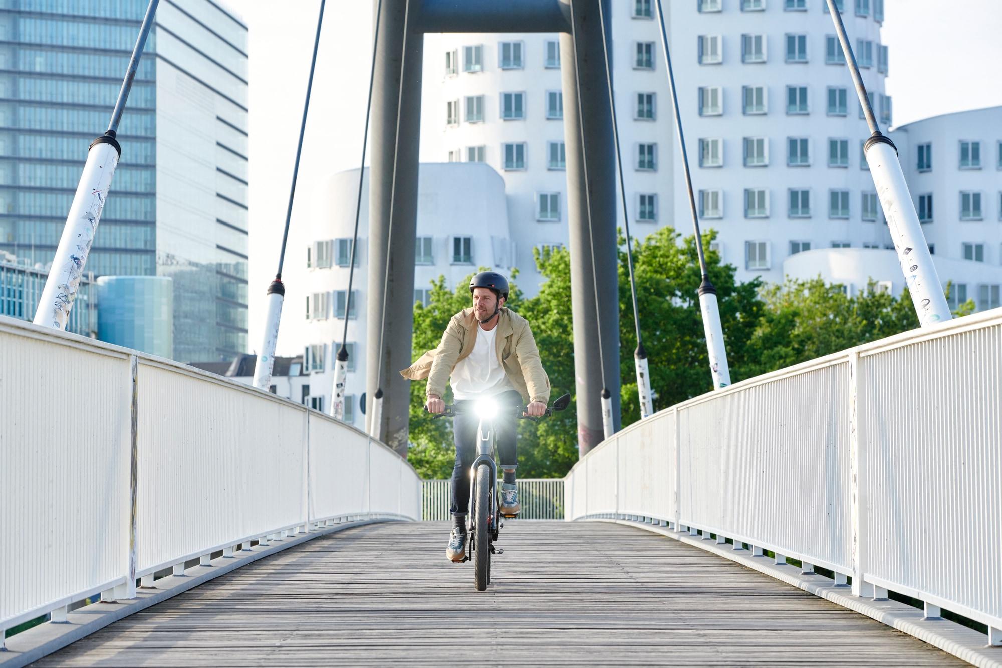 Ein Mann fährt mit einem E-Bike über eine Brücke in der Stadt. Perfekt für komfortable und umweltfreundliche Pendle
