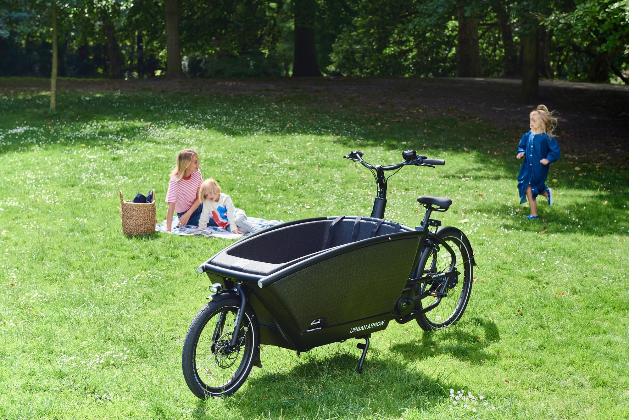 Urban Arrow Family auf der Wiese, auf einer Decke im Hintergrund Frau und Kinder