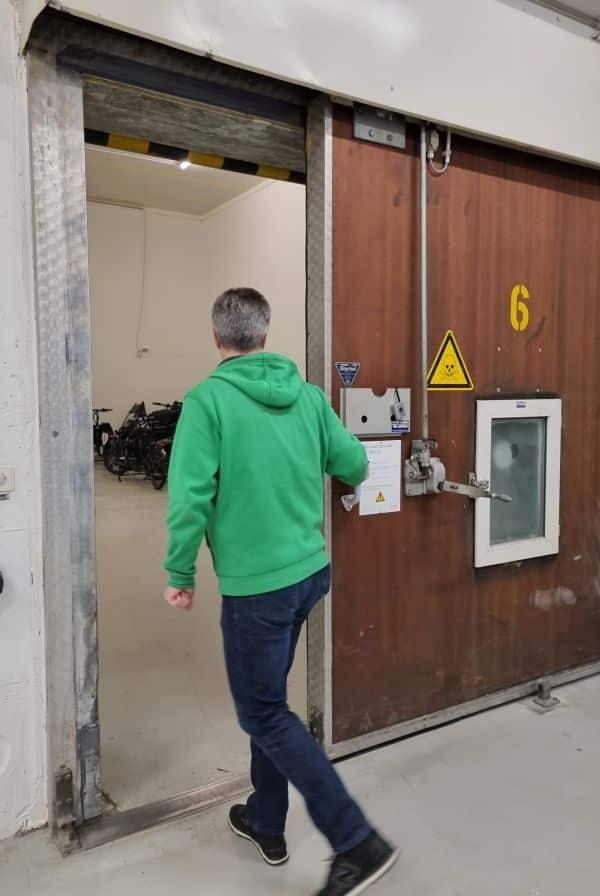 Mann öffnet schwere Metalltür zu Lagerraum mit Fahrrädern