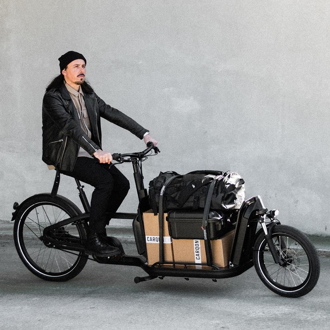 Ein Mann fährt mit einem vollgepackten Lastenrad, dem Carqon Flatbed, durch die Straßen