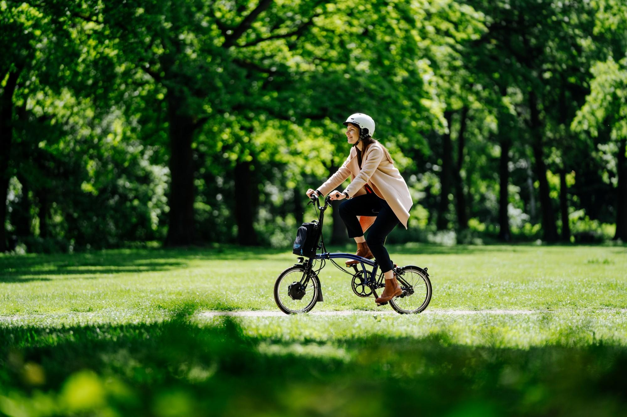 Frau fährt mit dem Brompton Falt-e-Bike durch den Park