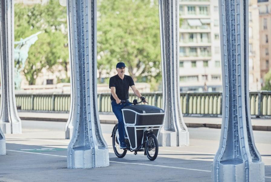 Mann fährt Lastenfahrrad unter Brücke in Stadtumgebung