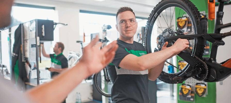 Mitarbeiter wartet Fahrrad in Werkstatt mit Ersatzteilen im Hintergrund