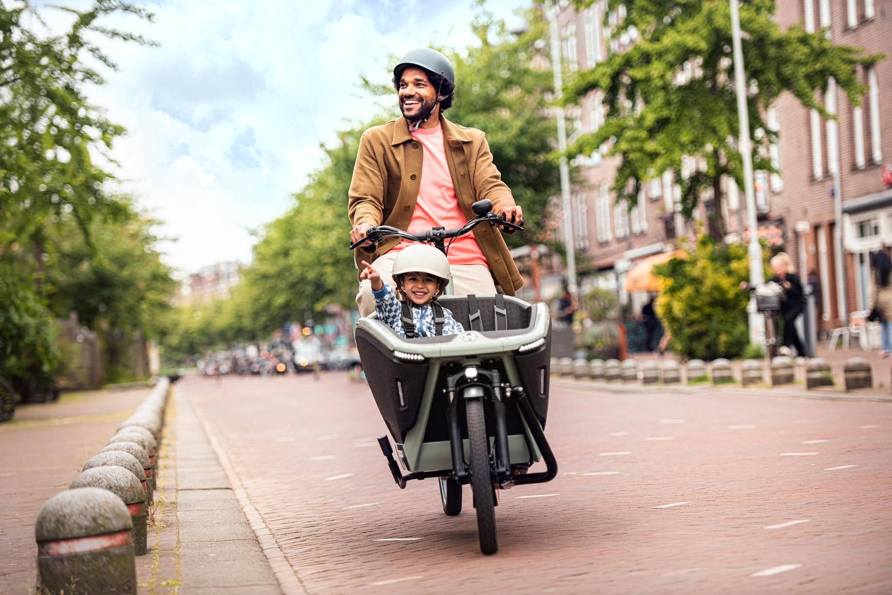 Ein Mann fährt sein Kind im Lastenrad von Urban Arrow durch die Straßen