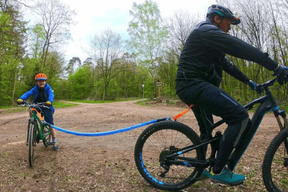 Ein Mann auf dem e-Bike zieht ein Kind auf dem Bike mit einem Abschleppseil