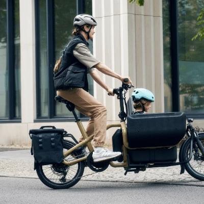 Mann fährt Riese & Müller Lastenrad mit Kindersitz auf Stadtstraße