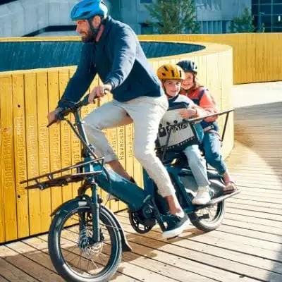 Vater mit Kindern auf einem E-Bike unterwegs auf Holzweg