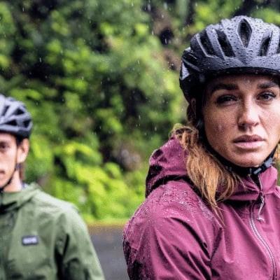 Zwei Personen mit Fahrradhelmen im Regen vor grüner Waldkulisse