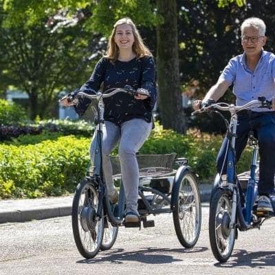 Zwei Personen fahren auf Dreirädern auf einer sonnigen Straße