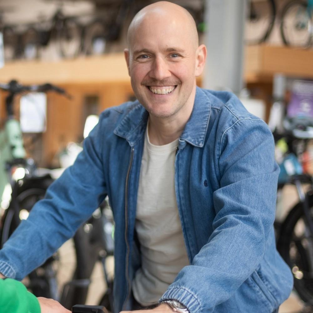 e-Bike Beratung. Mitarbeiter und Kunde lächeln zufrieden in die Kamera