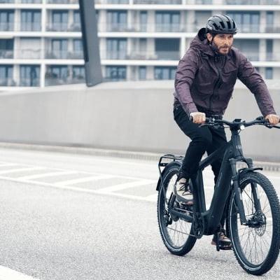 Mann auf E-Bike fährt über moderne Brücke in urbaner Umgebung