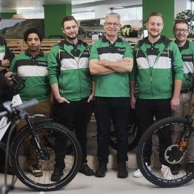 Teamfoto in Fahrradgeschäft mit E-Bikes und Mitarbeitern in grüner Kleidung