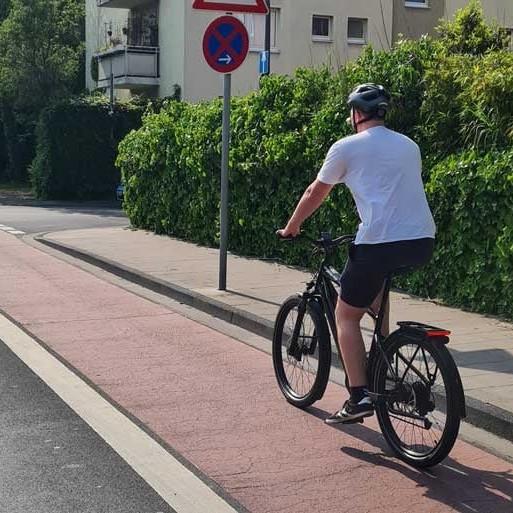 Radfahrer auf Radweg mit Verkehrsschildern und grüner Hecke