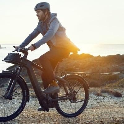 Mann fährt Riese & Müller Charger3 E-Bike am Strand bei Sonnenuntergang