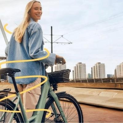 Frau mit E-Bike auf Brücke bei Sonnenuntergang in urbaner Umgebung