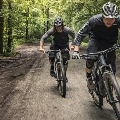 Zwei Mountainbiker fahren dynamisch auf Waldweg